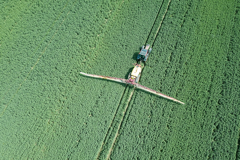 Aerial view Farm machinery spraying chemicals on a large green field