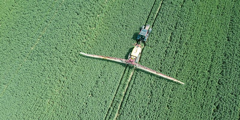 Aerial view Farm machinery spraying chemicals on a large green field