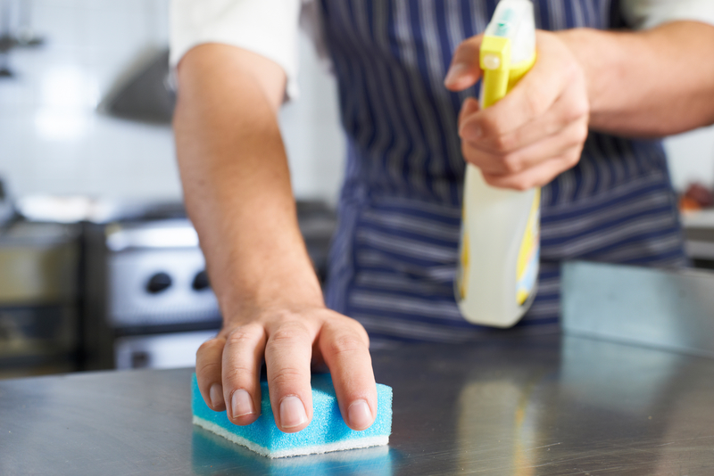 Close Up Of Worker In Restaurant Kitchen cleaning down a surface